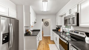 A modern kitchen with stainless steel appliances, white cabinetry, and a wooden floor.