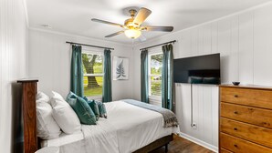 A bedroom with a bed, a wooden dresser, a ceiling fan, and a TV.