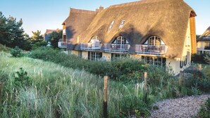 A thatched-roof house with a balcony, surrounded by greenery.