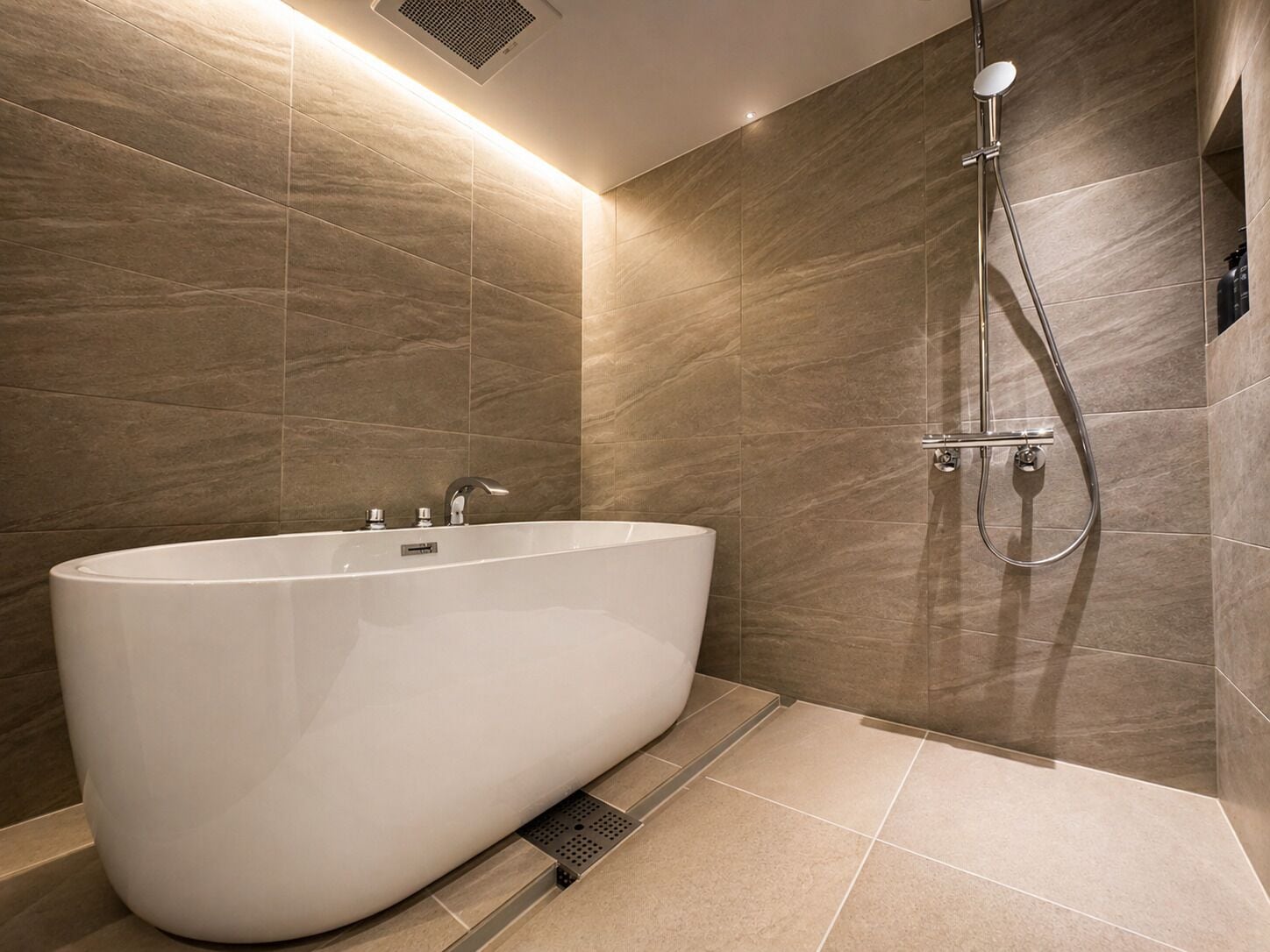 Un baño moderno con una bañera independiente, un cabezal de ducha manual y un grifo de pared.