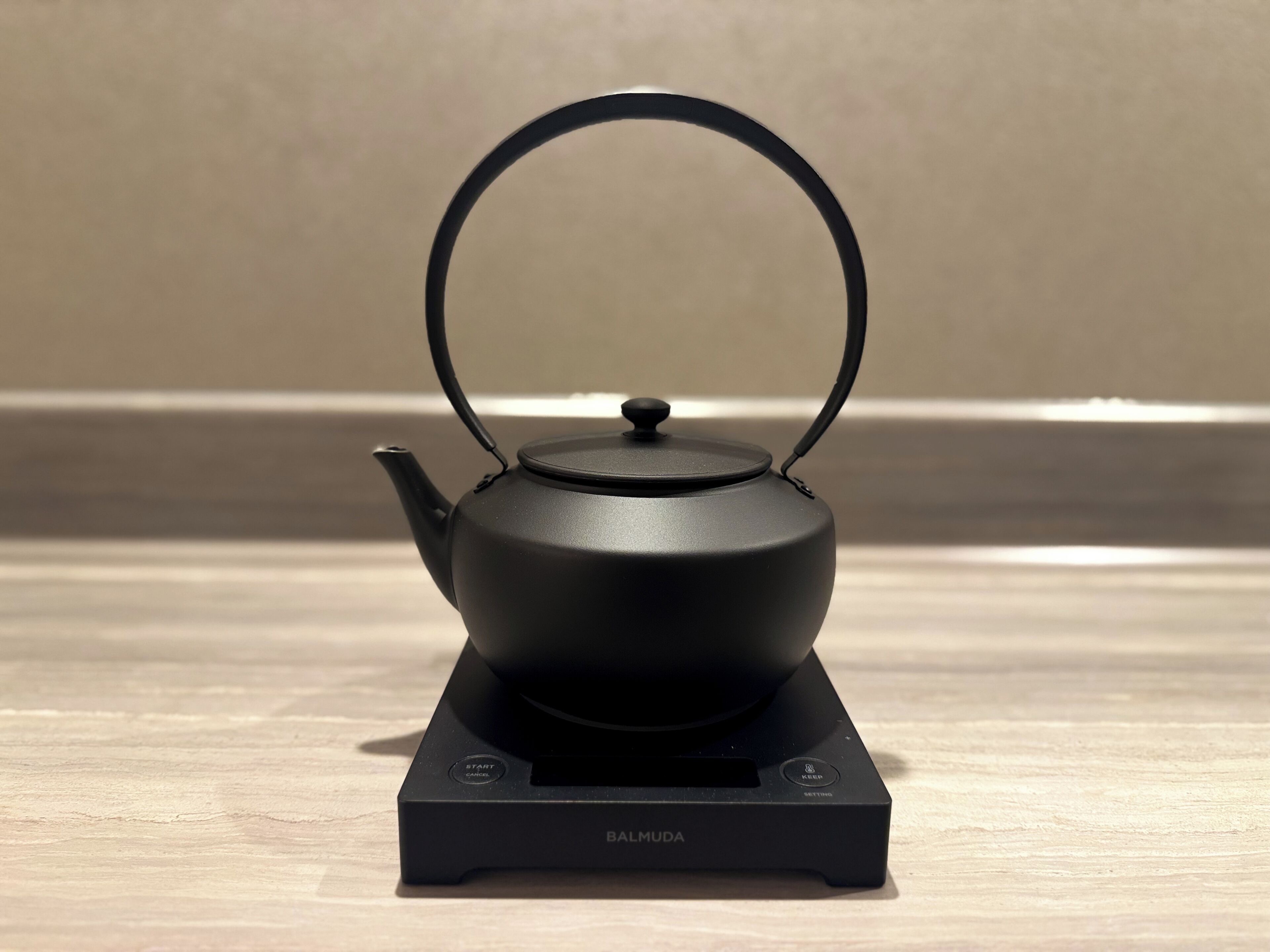 A black teapot on a stand with a label that reads 'BALMUDA.'