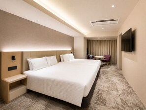 A hotel room with a large bed, bedside tables, a desk, a chair, a TV, and an air conditioning unit.
