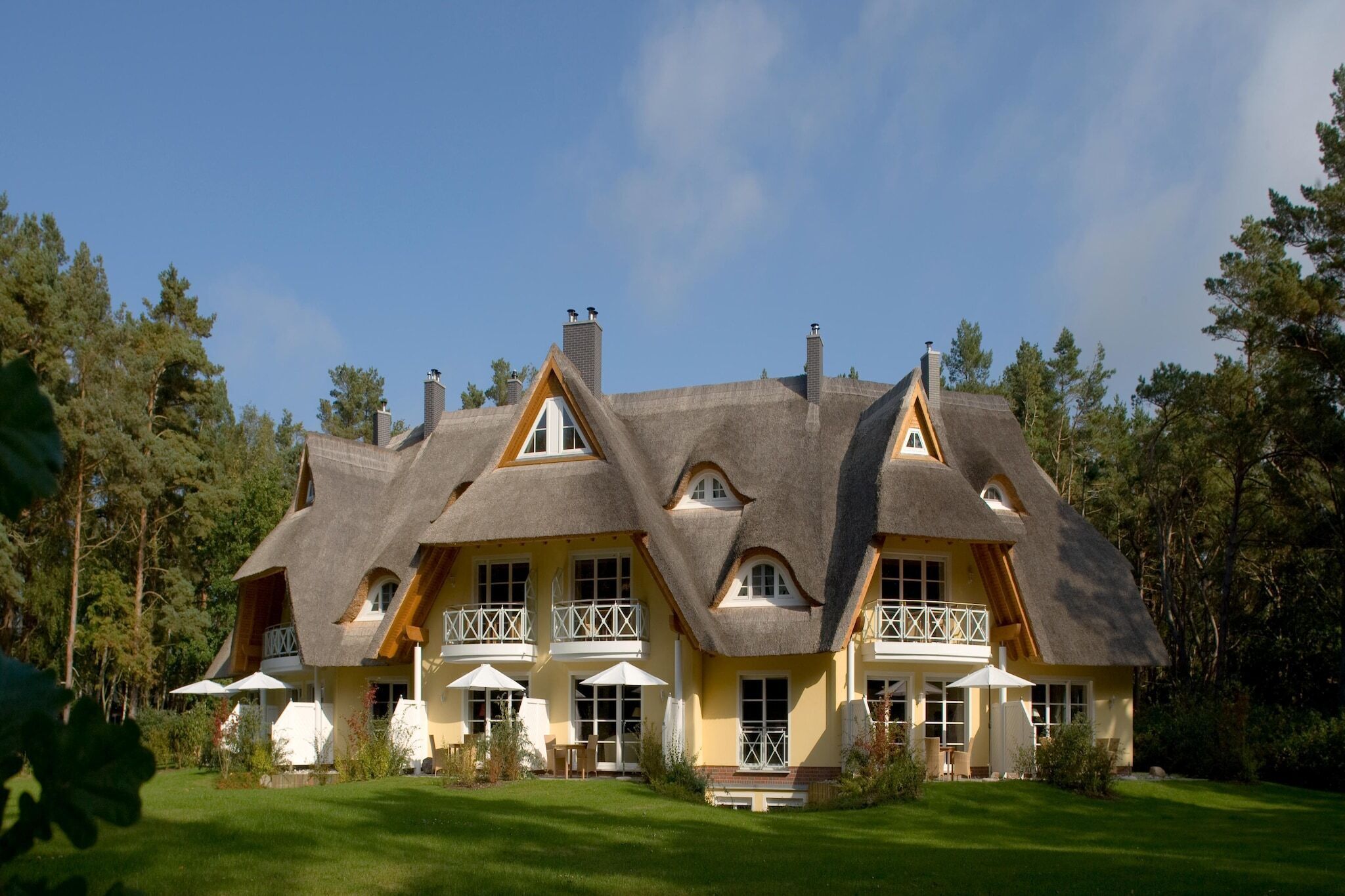 Ein großes, mehrgeschossiges Haus mit einem Strohdach, mehreren Balkonen und einem gepflegten Rasen.