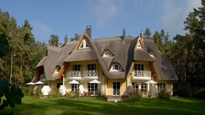 A large, multi-story house with a thatched roof, multiple balconies, and a well-maintained lawn.