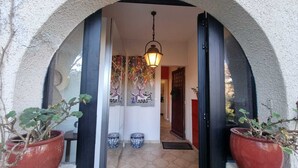 Una entrada arqueada con una lámpara colgante, plantas en macetas y un suelo de baldosas que conduce a una puerta.