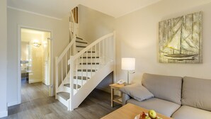 A modern living room with a wooden staircase, a sofa, a coffee table with fruit, and a wall-mounted lamp.
