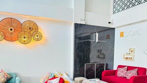 Uma sala de estar moderna com um sofá vermelho, uma poltrona amarela e um sofá azul. Há uma parede de mármore preto com uma placa 'ROOM LAVNA'.