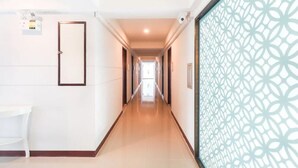 Corredor de hotel com um divisória estampada à direita, uma porta à esquerda e vista para um quarto no final.