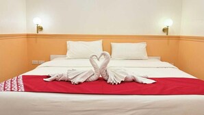 Una habitación de hotel con cama, dos almohadas blancas, una colcha roja y dos lámparas fijadas a la pared.
