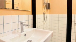 Un baño con un lavamanos blanco, un espejo y una ducha con cabezal de ducha manual.