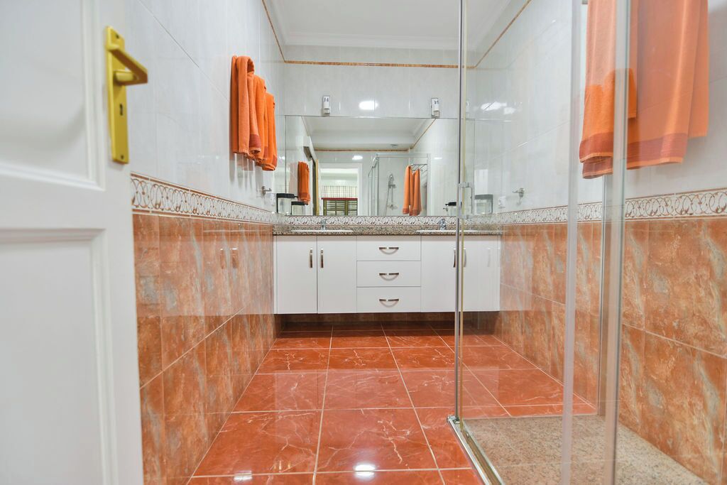 A bathroom with a glass shower enclosure, white cabinets, and orange towels.