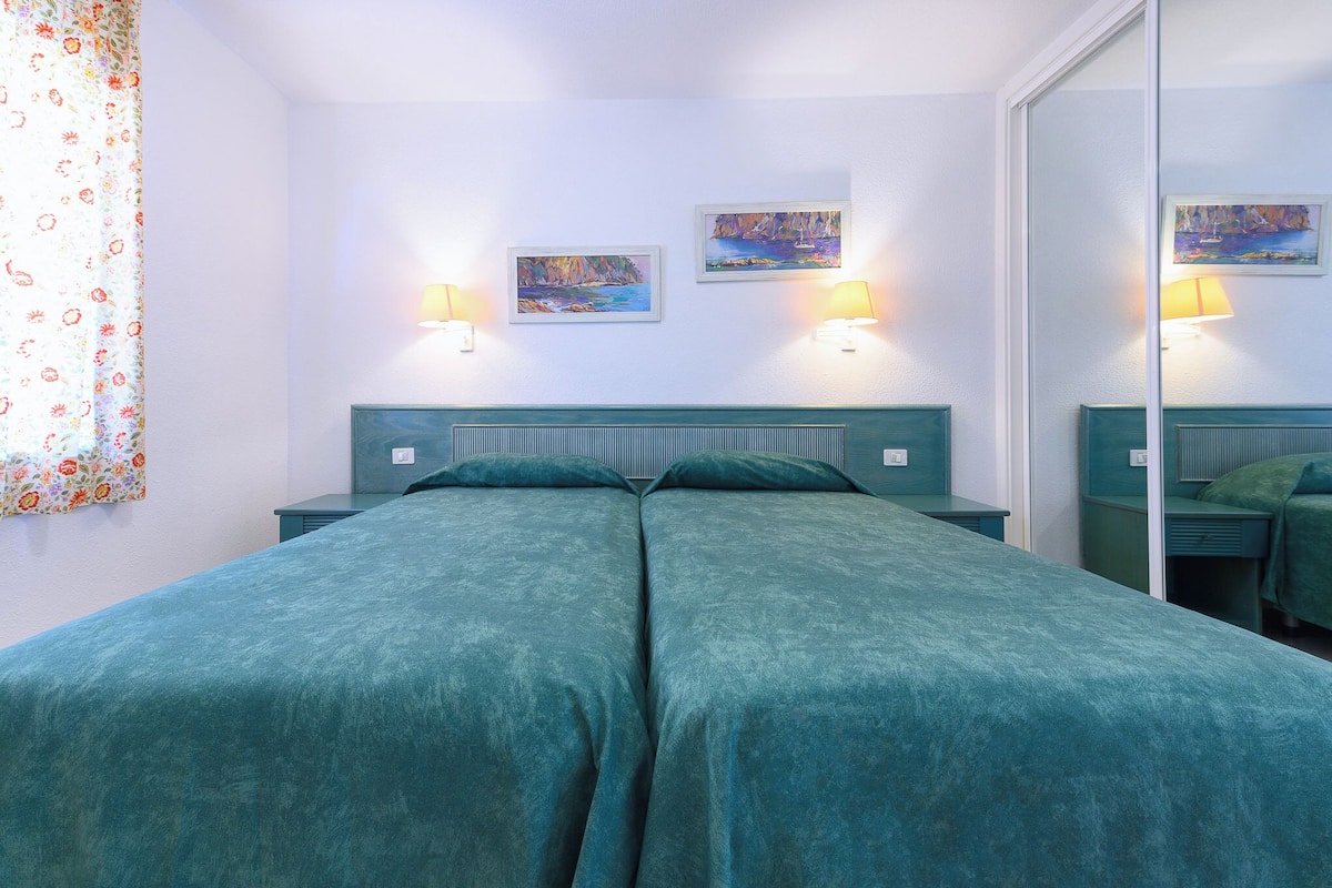 Una cama doble con colcha color turquesa, dos lámparas de pared y dos cuadros en la pared.