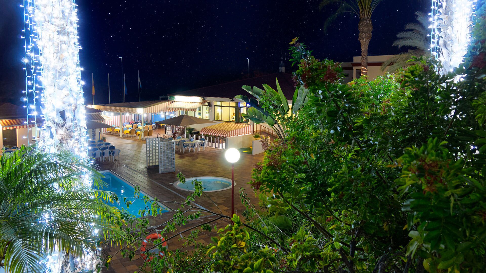 An outdoor pool area with a covered seating area and a building in the background.