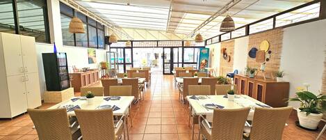 A spacious restaurant with high ceilings, large windows, and wicker furniture.