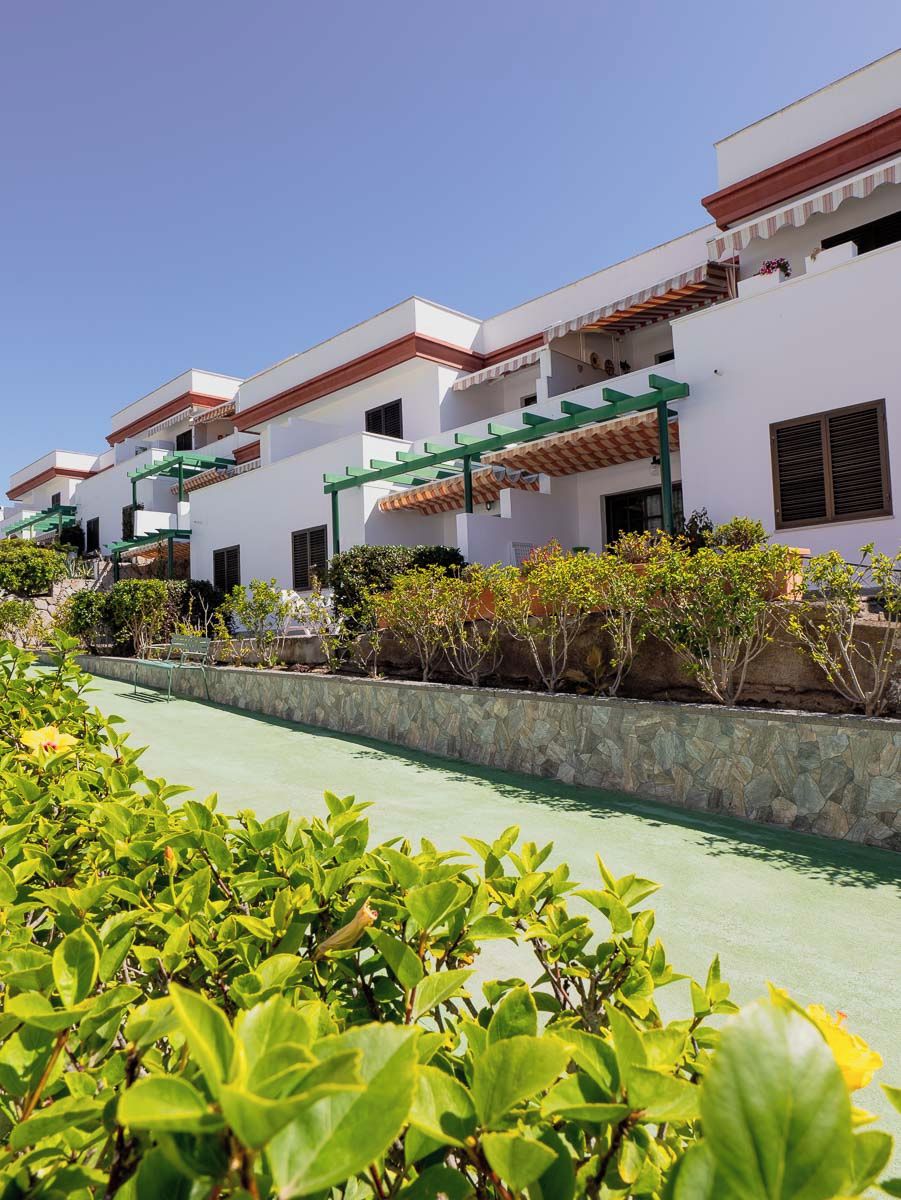 A row of white buildings with red roofs and green awnings, a stone wall, and a green pathway.