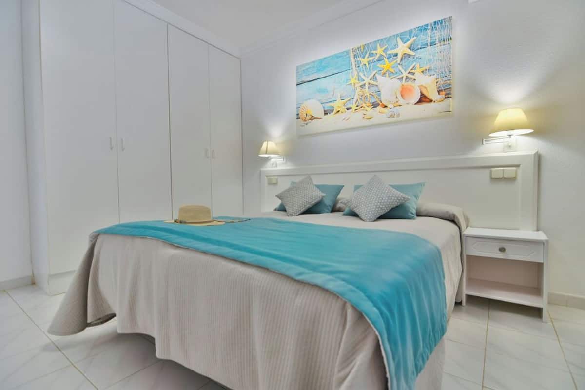 Un dormitorio con cama, mesitas de noche, un armario y un cuadro colgado en la pared.
