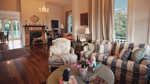 Un salón amplio con chimenea, un conjunto de sofás, un sillón con estampado floral y una mesa de centro con adornos.