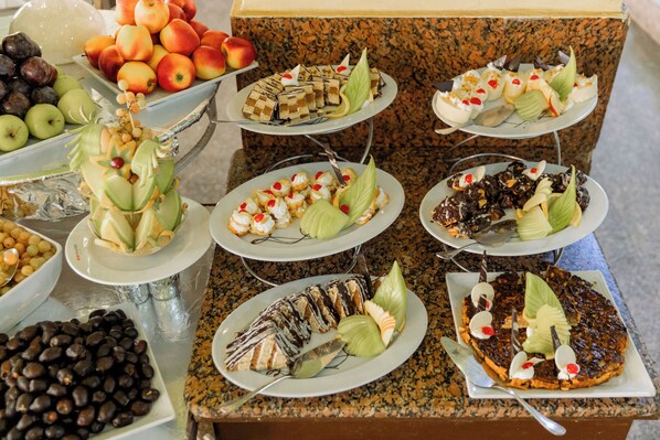 Un bufé con diversos platos, incluyendo frutas, postres y frutos secos.