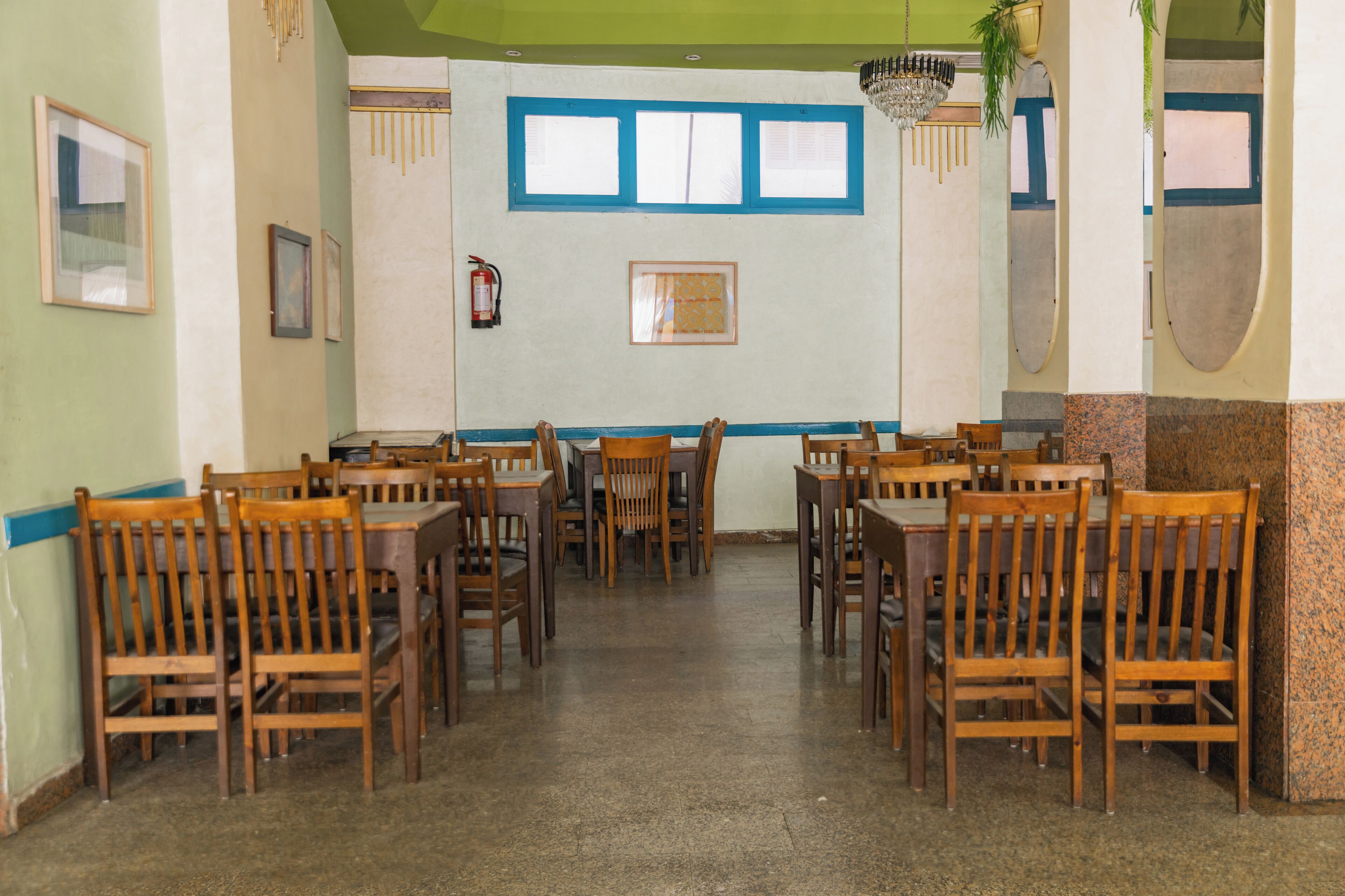 A dining area with wooden tables and chairs, a fire extinguisher, and framed pictures on the walls.