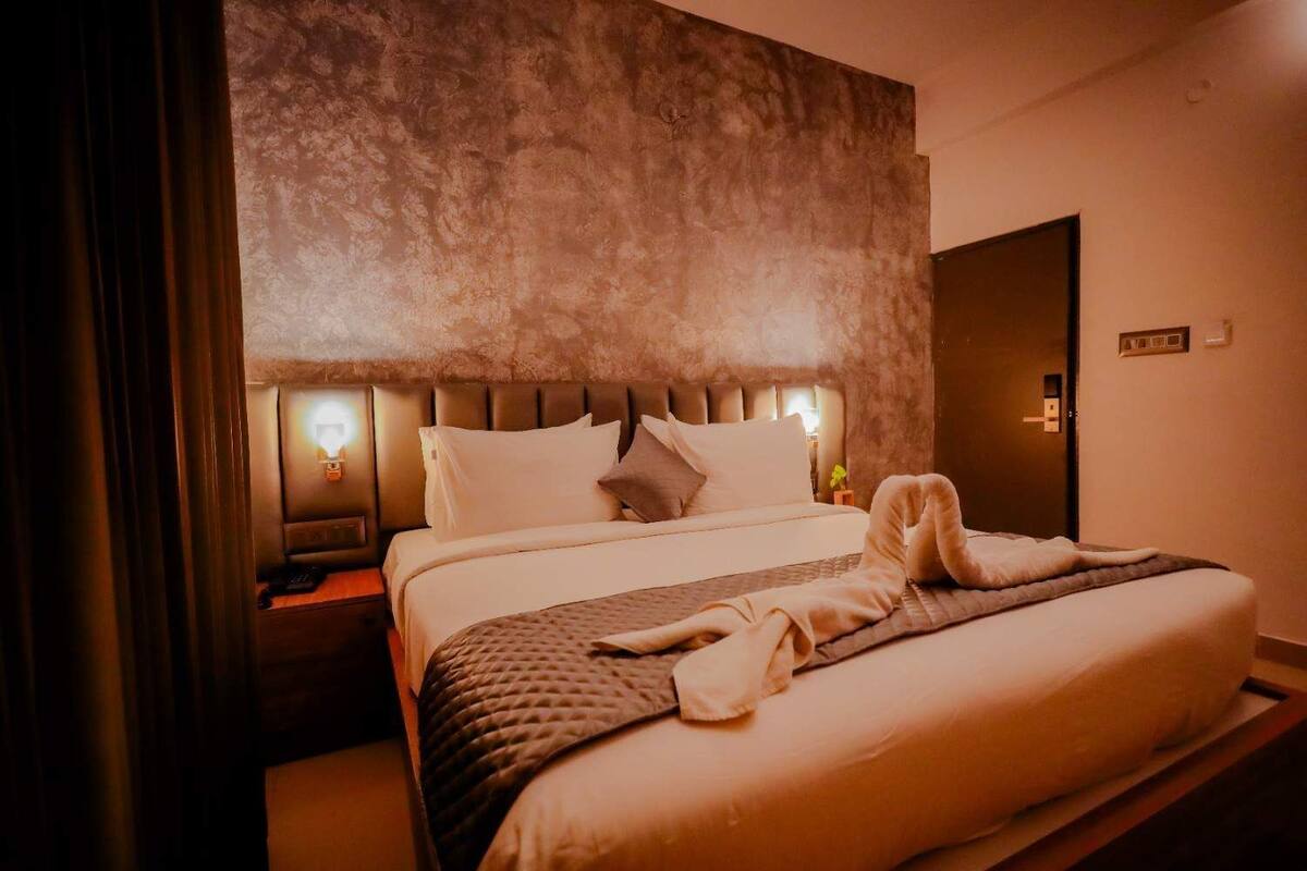 Ein Hotelzimmer mit einem großen Bett, einem Kopfteil mit integrierter Beleuchtung, einem Nachttisch und einer Tür.