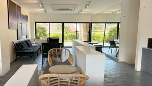 A modern interior with a seating area featuring wicker chairs and a sofa, large windows offering a view of greenery, and a clean, minimalist design.
