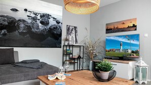 Ein modernes Wohnzimmer mit einer Couch, einem Holztisch und einem Fernseher. An den Wänden befinden sich Gemälde und eine Bücherwand mit Büchern und Dekoration.