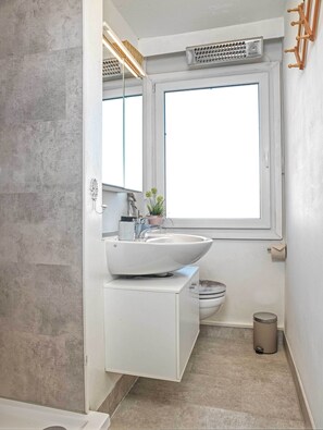 Ein modernes Badezimmer mit großem Fenster, einem weißen Waschbecken und einer Toilette.