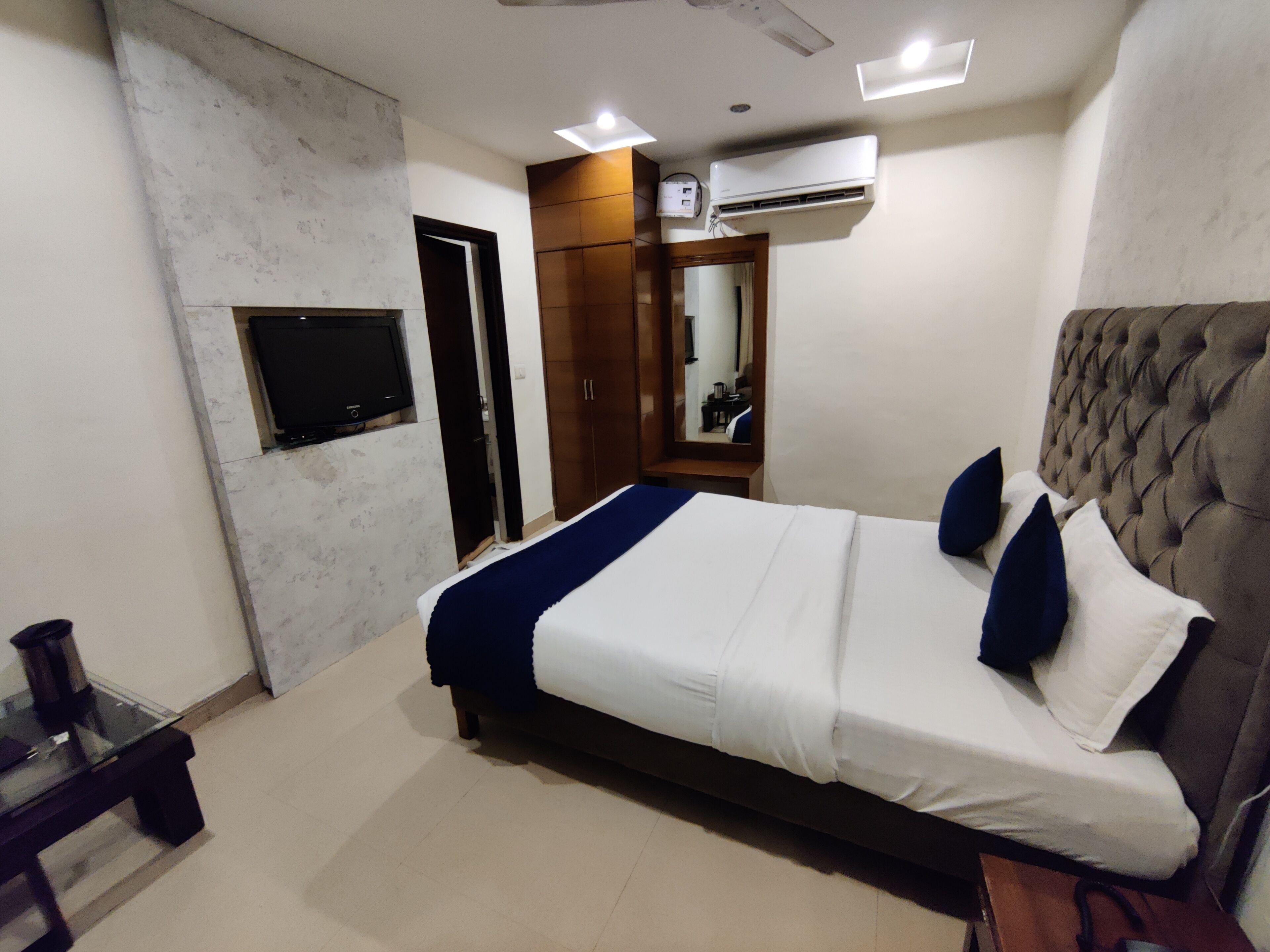 Une chambre moderne avec un grand lit, un téléviseur fixé au mur, un appareil de climatisation et une armoire.