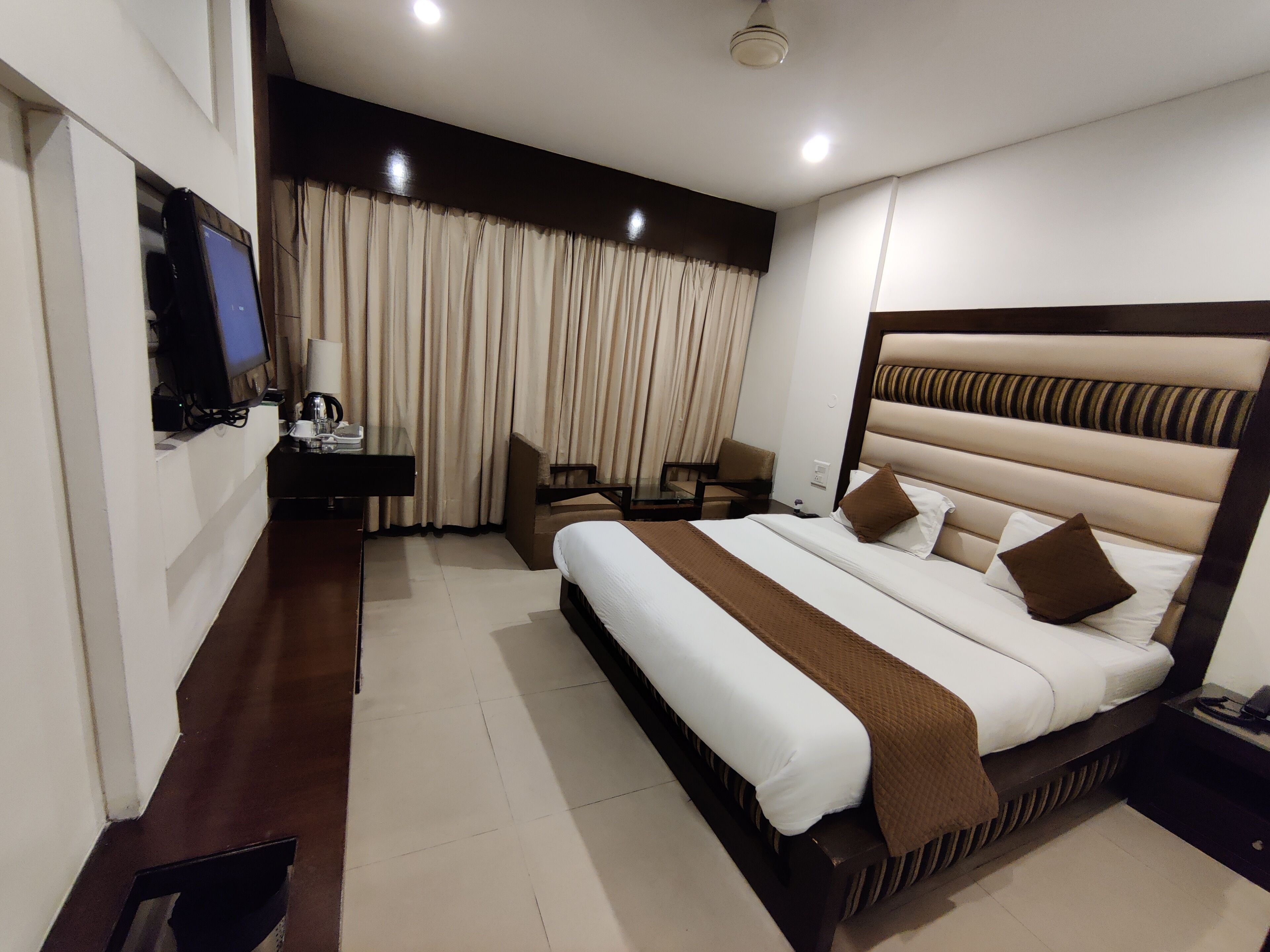A hotel room with a large bed, a desk with a computer, a chair, and a television.