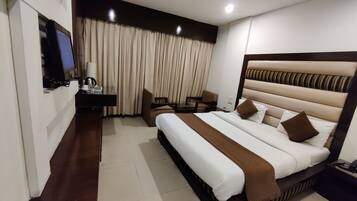 A hotel room with a large bed, a desk with a computer, a chair, and a television.
