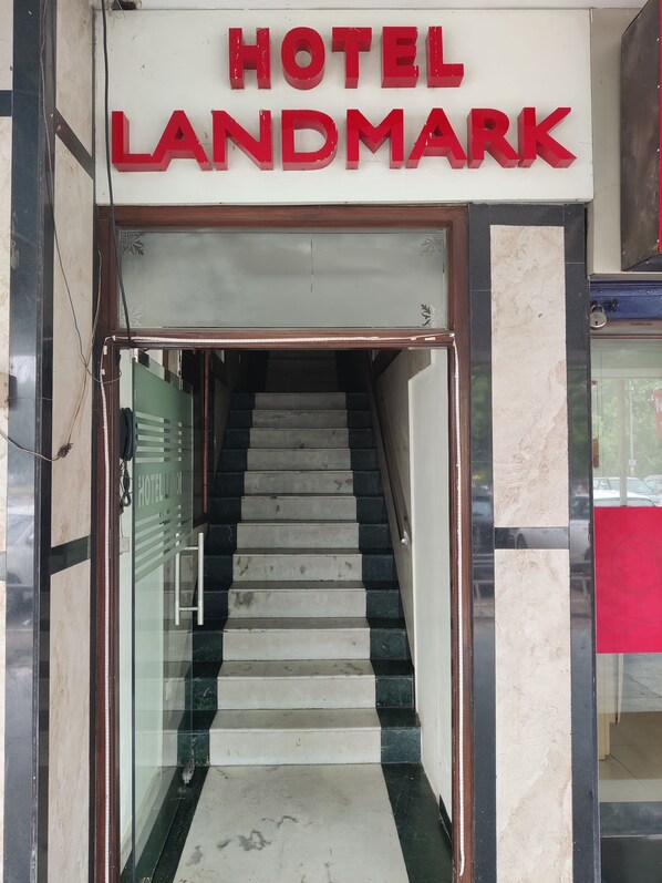 Uma escadaria leva à entrada de um hotel, com uma placa que diz 'HOTEL LANDMARK'.