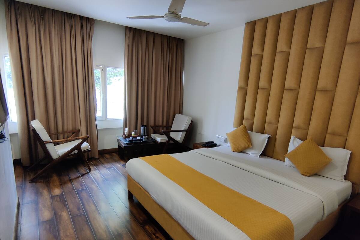 A hotel room with a large bed, a desk, a chair, a ceiling fan, and a window with curtains.
