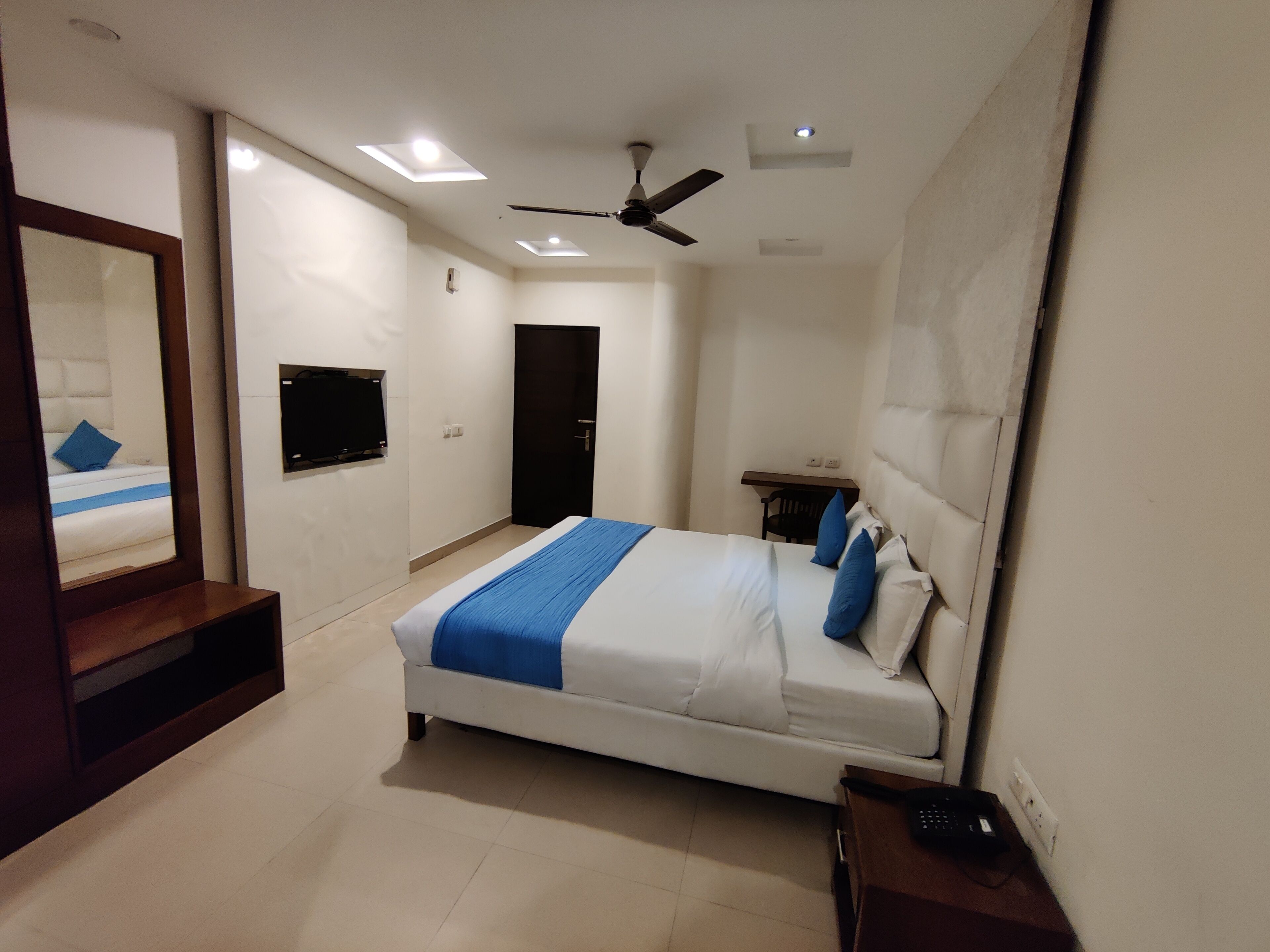 Une chambre à coucher avec un lit, un ventilateur de plafond, une télévision et une porte.