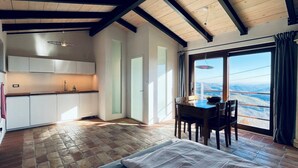 A compact kitchen with white cabinets and a dining area with a table and chairs. A large window offers a view of the landscape. - Villa MOKA, modern STUDIO in a farmhouse (15th cent.);  Montefeltro (Le Marche) (Lunano)