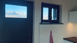 A room with a dark door, a window with a view of mountains, a white cabinet, and a towel hanging on a hook. - Villa MOKA, modern STUDIO in a farmhouse (15th cent.);  Montefeltro (Le Marche) (Lunano)