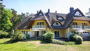 Ein zweistöckiges Haus mit einem Strohdach, einem Balkon und einem gepflegten Garten.