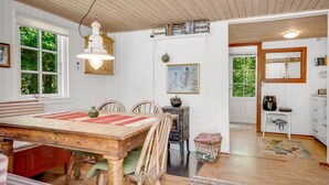 Un comedor acogedor con una mesa de madera, sillas y un mantel individual rojo. Se ve una ventana con vistas a zonas verdes y una pequeña cocina con un fregadero y armarios.