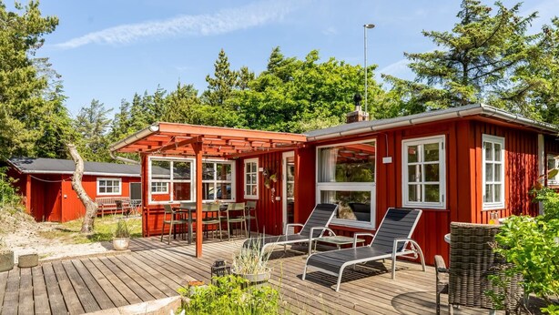 Una cabaña de madera roja con un porche, mobiliario exterior y un pequeño jardín.