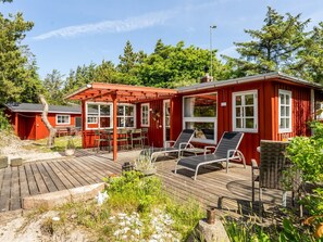Eine rote Holzhütte mit einer Terrasse, Sitzgelegenheiten im Freien und einem kleinen Garten.