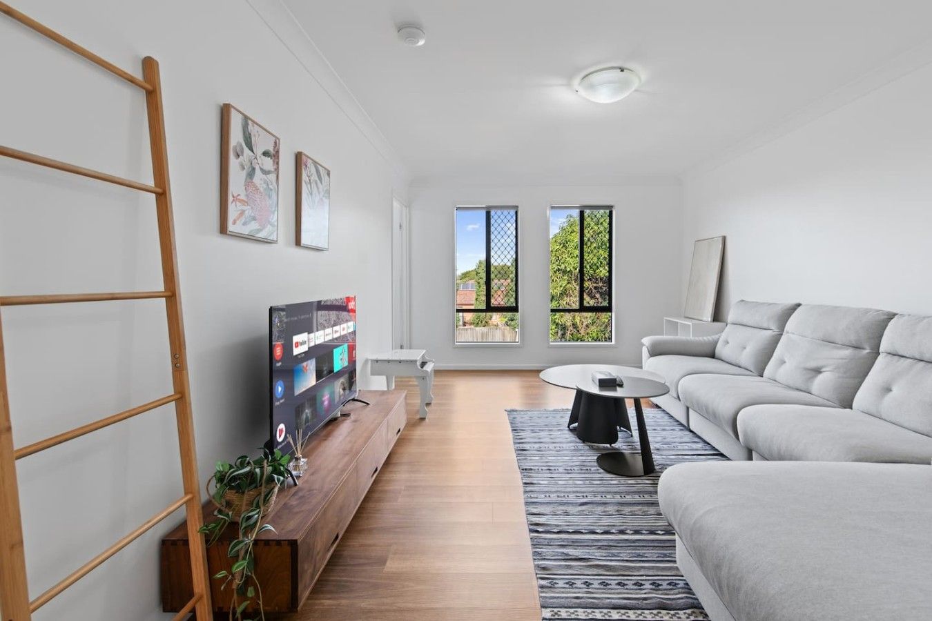 A modern living room with a flat-screen TV, a grey sofa, a coffee table, and a wooden TV stand.