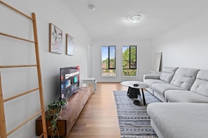 Una sala de estar moderna con un televisor de pantalla plana, un sofá gris, una mesa de centro y un mueble de televisión de madera.