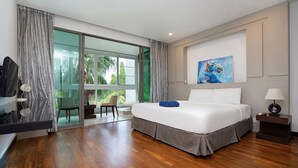 A modern bedroom with a large bed, a sliding glass door leading to a balcony, a painting on the wall, and a nightstand with a lamp. - Elegant 2BR Apartment RGN B411 in Laguna (Choeng Thale)