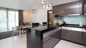 A modern kitchen with a central island, stainless steel appliances, and a dining area with a table and chairs. - Elegant 2BR Apartment RGN B411 in Laguna (Choeng Thale)