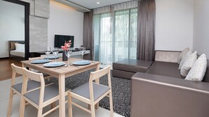 A modern living room with a dining area, a sofa, and a television. - Elegant 2BR Apartment RGN B411 in Laguna (Choeng Thale)