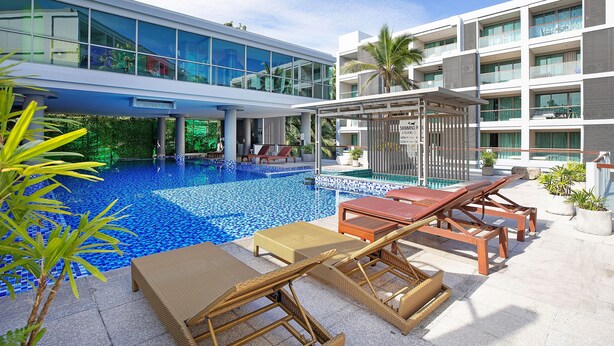 A modern hotel with a rooftop pool, lounge chairs, and a glass facade. - Elegant 2BR Apartment RGN B411 in Laguna (Choeng Thale)