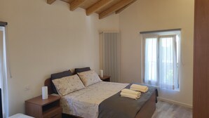 Un dormitorio con cama, mesitas de noche, una ventana con cortinas y techo de madera.