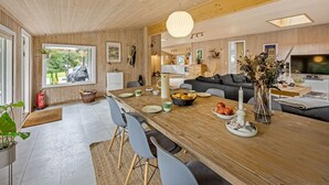 Eine moderne Küche mit Holzschränken, eine Essecke mit Holztisch und -stühlen, ein Sofa und ein Fernseher.