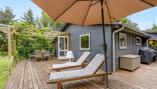 Eine Holzterrasse mit Liegestühlen und einer Pergola, ein Patio-Tisch sowie ein Grillbereich.