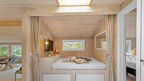 Ein gemütliches Schlafzimmer in einer Holzhütte mit Bett, Nachttisch und Fenster.