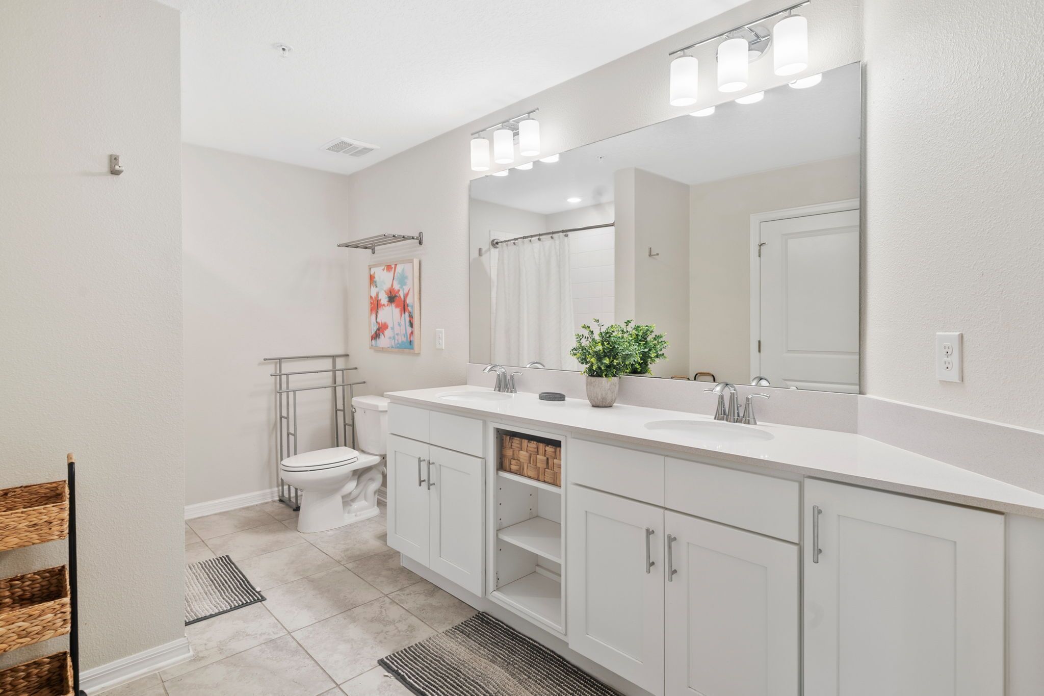 A modern bathroom with a large mirror, white cabinetry, and a shower area.
